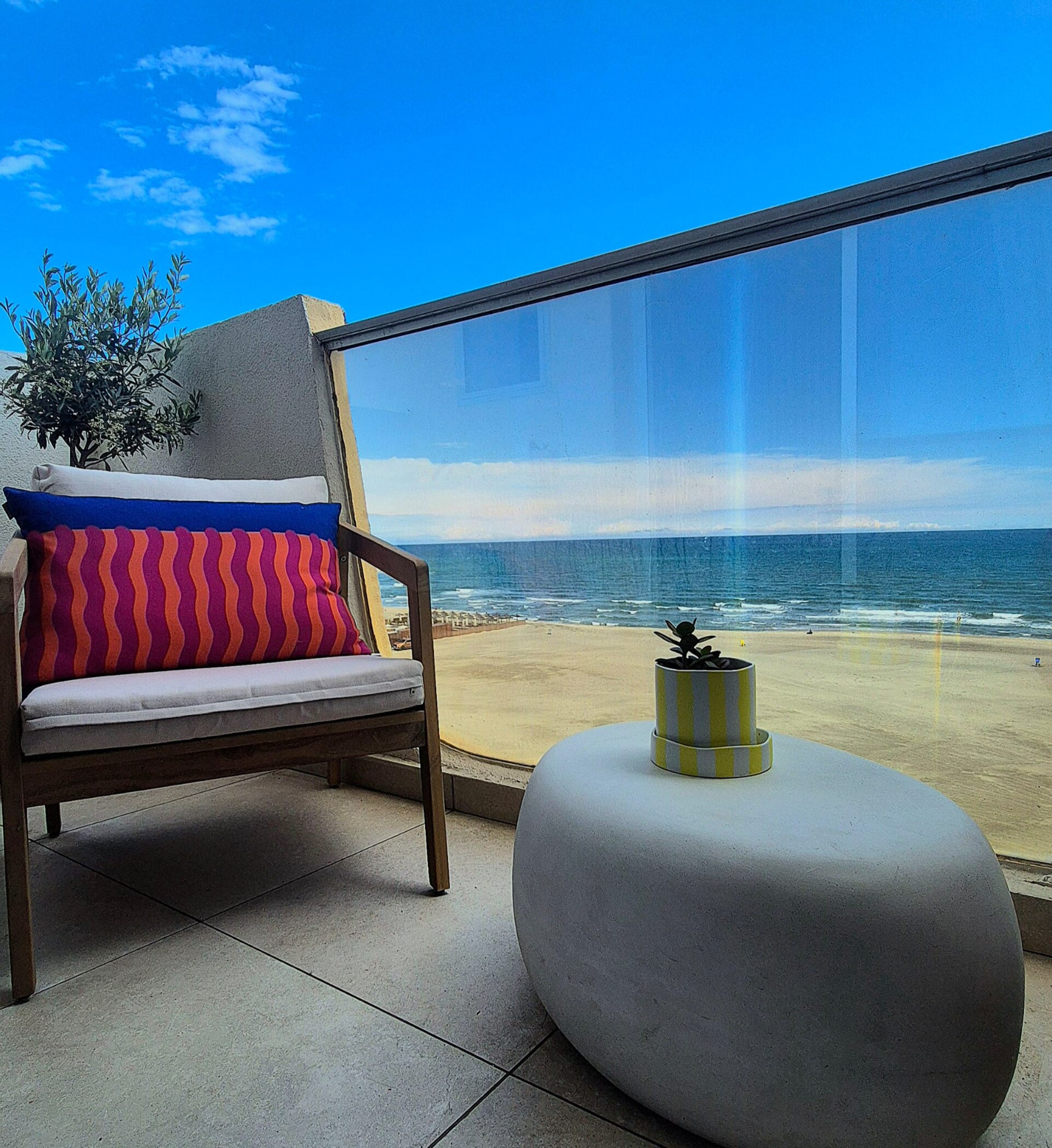 Terrasse ensoleillée avec fauteuil et coussin rayé face à la mer